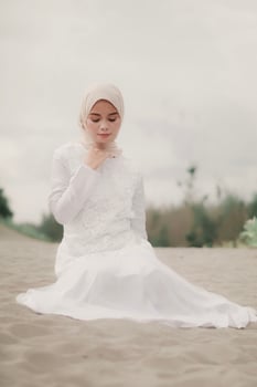 Beautiful islamic female model wearing hijab fashion, a modern wedding dress for muslim woman sitting in the sand and beach. Portrait an asian girl model using hijab having fun at the beach with trees photo