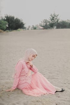 Beautiful islamic female model wearing hijab fashion, a modern wedding dress for muslim woman sitting in the sand and beach. Portrait an asian girl model using hijab having fun at the beach with trees photo