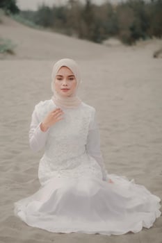 Beautiful islamic female model wearing hijab fashion, a modern wedding dress for muslim woman sitting in the sand and beach. Portrait an asian girl model using hijab having fun at the beach with trees photo