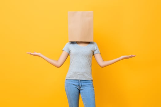 Anonymous woman in casual attire cover head with paper bag doing open hand gesture in yellow studio background photo