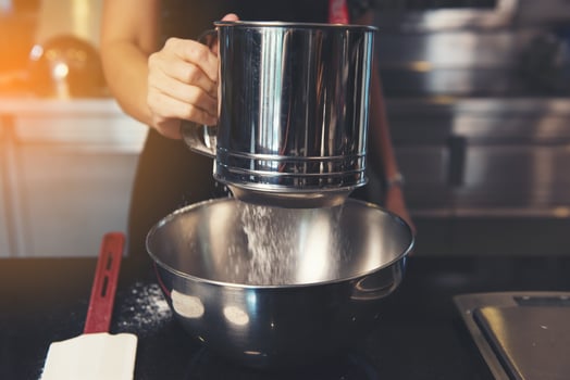 hand sifting flour powder from sieve on black kitchen table photo