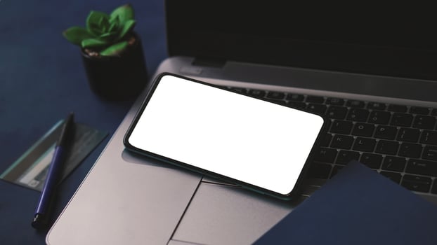 Mobile phone mockup template with white screen on a laptop for remote working and home office concept photo
