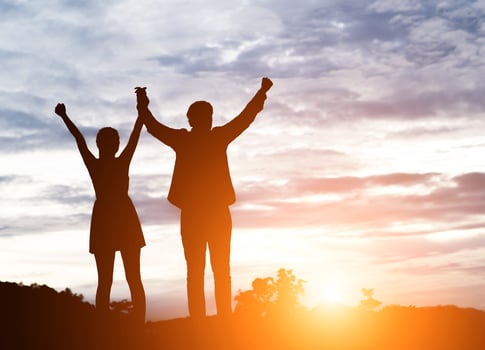 Silhouette of young couple together arms up in the air of happiness with accomplishment in the clouds at sunset. photo