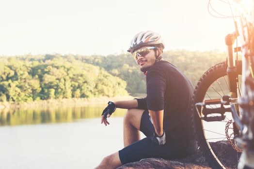 Young athlete man sitting on a rock with bicycle enjoy with nature of lake during sunset. photo