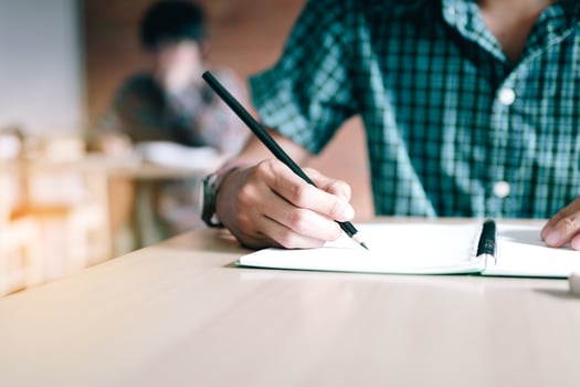 Close up of student hand writing on paper with a pencil in classroom. photo