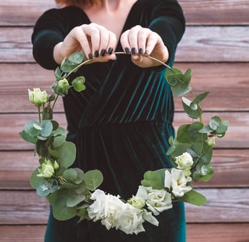 Female hands holding a decorated wreath of flowers and leaves on a wooden background photo