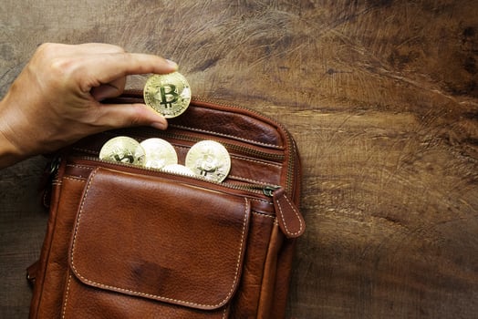The man's hand is picking up bitcoins money are contained in brown leather bags on wood desk very shiny. Design concept for business and trading photo