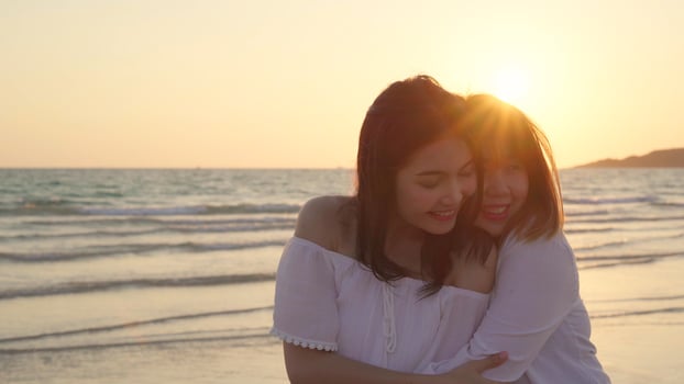 Young Asian lesbian couple kissing near beach. Beautiful women lgbt couple happy relax enjoy love and romantic moment when sunset in evening. Lifestyle lesbian couple travel on beach concept. photo