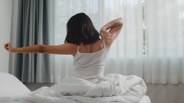 Teen hispanic woman wakes up at home. Young Asian girl stretching after awake sleep all night starting a new day with energy and vitality felt very refreshed on bed near window in bedroom at morning. photo