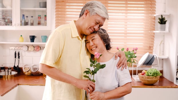 Asian elderly couple feeling happy smiling and holding flower and looking to camera while relax in kitchen at home. Lifestyle Senior family enjoy time at home concept. Portrait looking at camera. photo