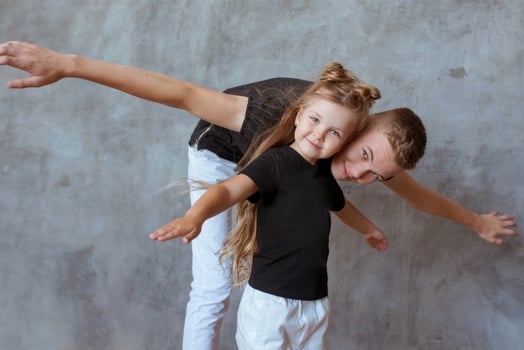 caucasian siblings - teenager boy brother and little girl sister playing in aircraft in modern loft interior on gray cement background photo