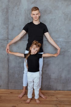 stylish caucasian siblings in blak t-shirts and white pants standing by the gray wall in loft interior. Family, fashion, relatives, relationship and children concept. photo