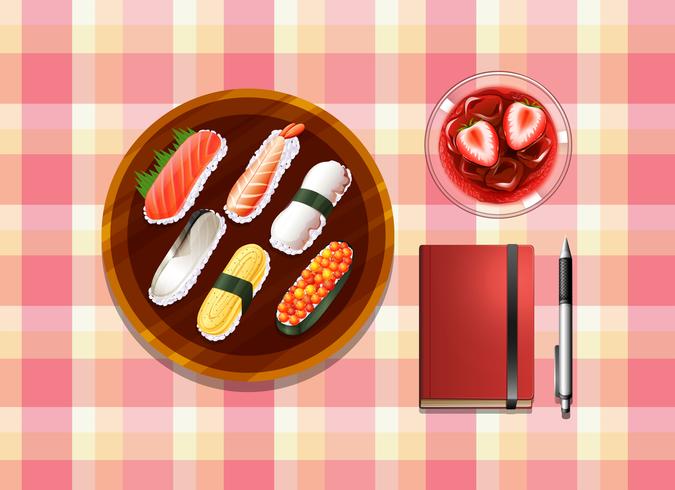 A table with sushi, a cocktail drink, a ballpen and a notebook