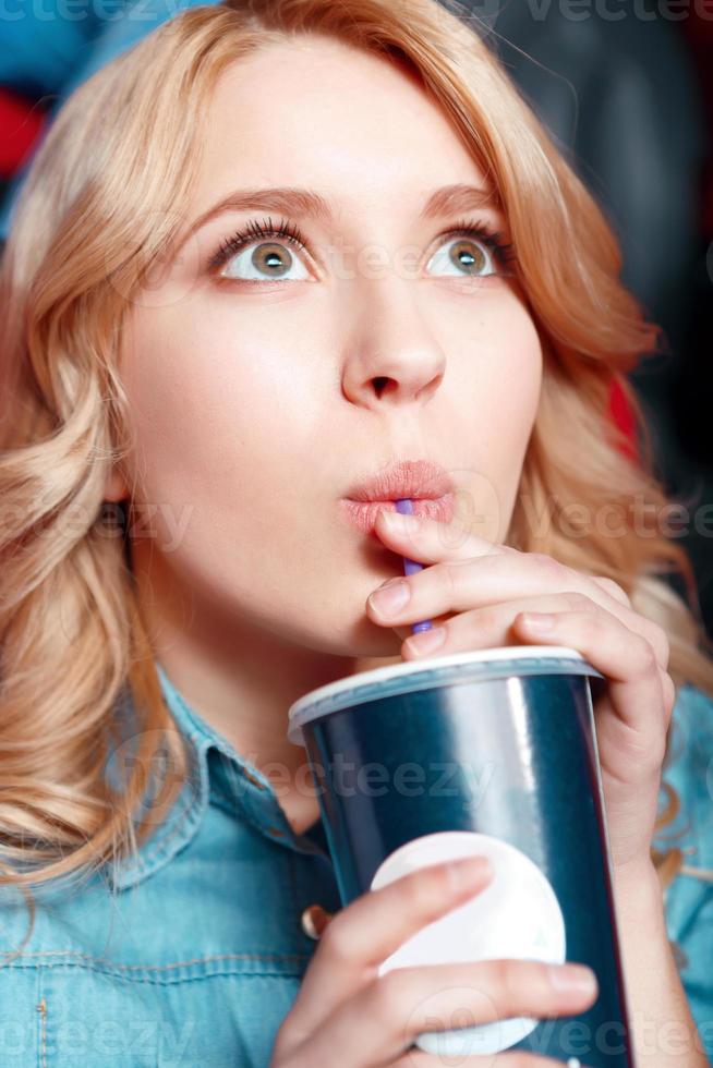 Young woman enthusiastically drinking coke in cinema photo