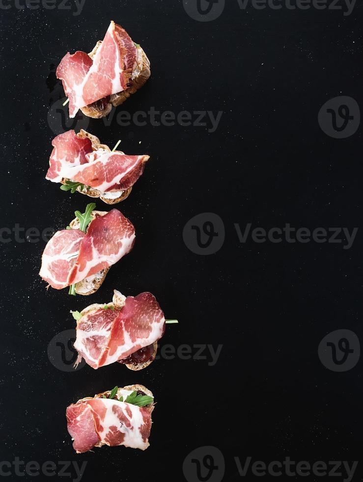 Bruschettas with prosciutto smoked meat, dried tomatoes and arugula over photo