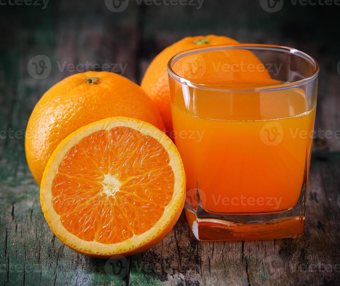 vaso de jugo de naranja y naranjas frescas en madera foto