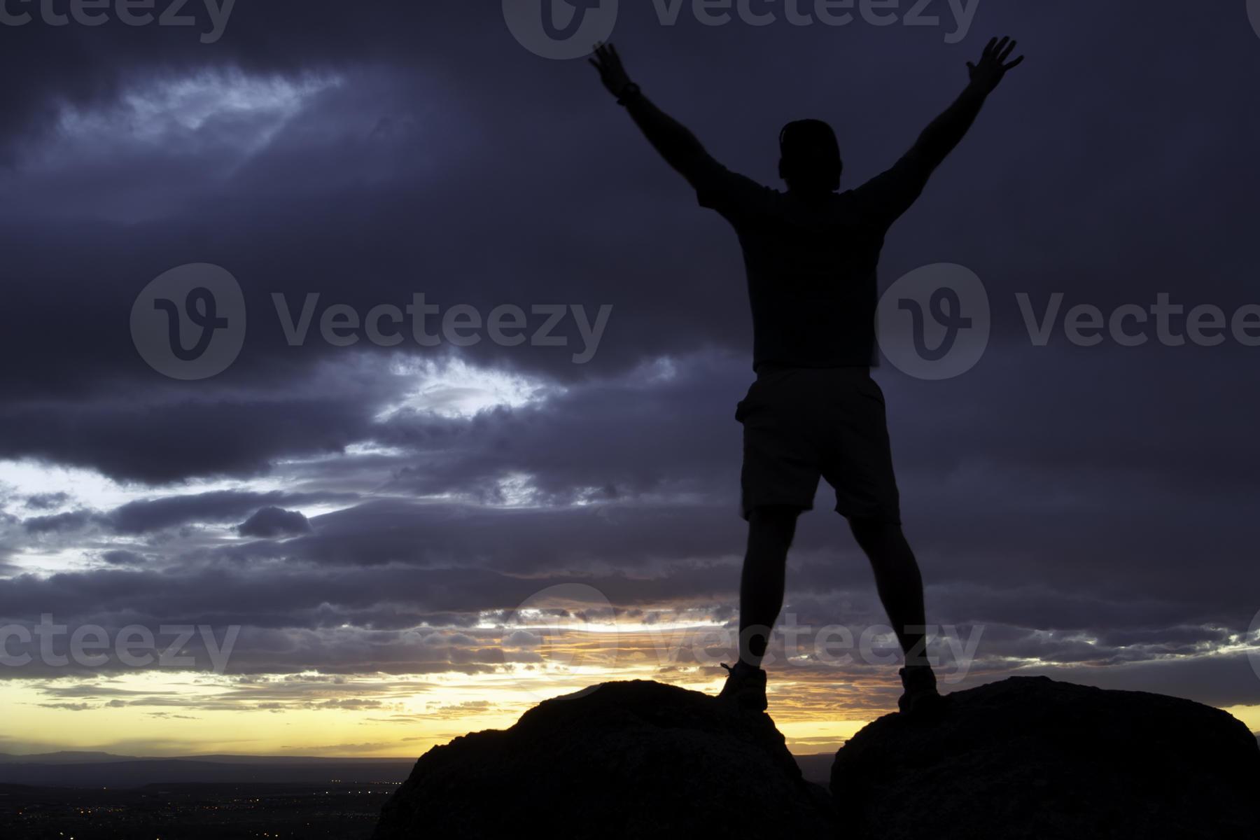 silhouette man with arms raised into sunset sky landscape photo