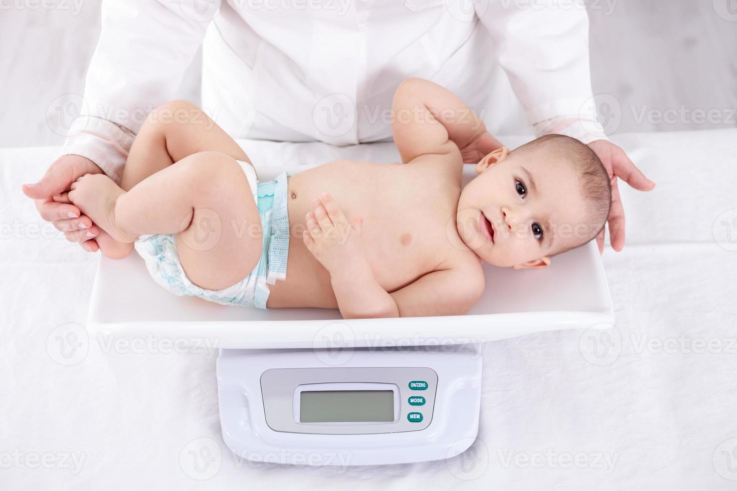 Pediatra de sexo femenino que pesa al bebé en la oficina foto