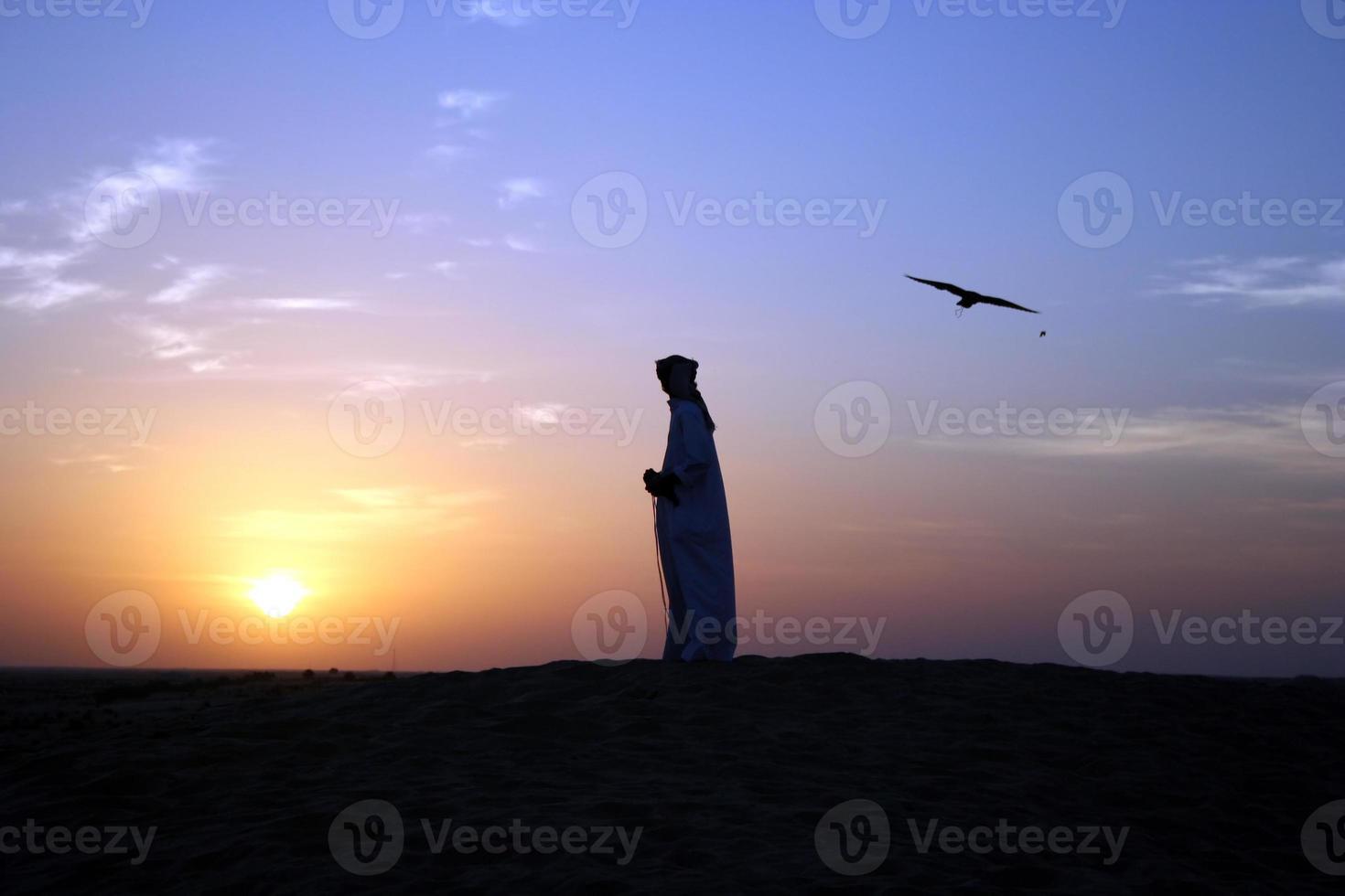 Silhouettes of an Arabian man and a bird at sunset photo