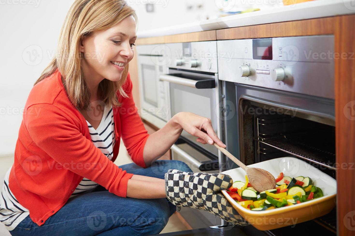 Mujer poniendo la bandeja de verduras asadas en el horno foto