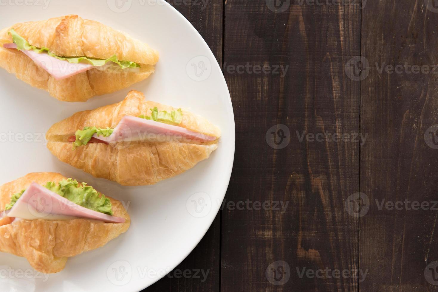 Croissant with parma ham and lettuce on wooden table photo