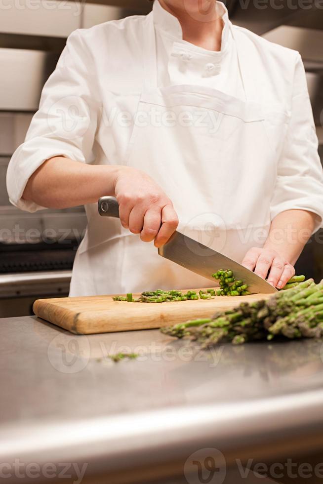 Female chef chopping asparagus in commercial kitchen photo