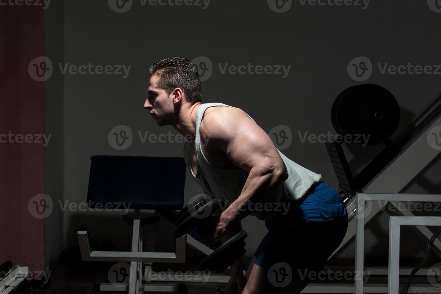 Hombre en el gimnasio ejercitando tríceps con mancuernas foto