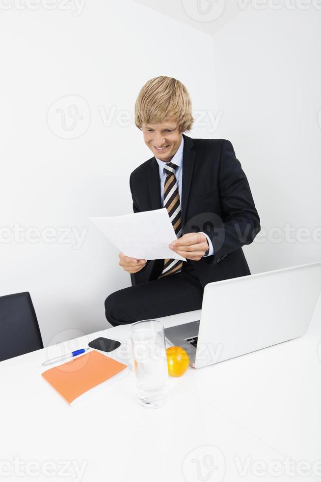 Sonriente hombre de negocios adulto medio documento de lectura con laptop foto