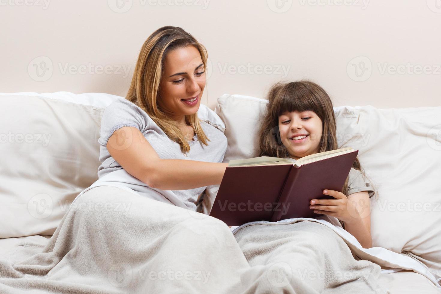 Mother and daughter reading together book in bed photo