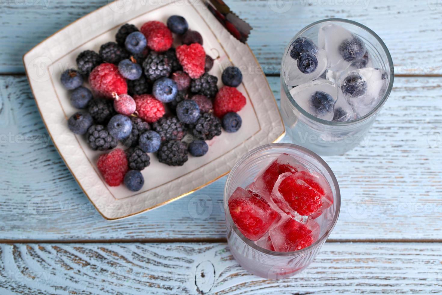 Frozen berries and ice cubes, raspberry and blueberry on table photo