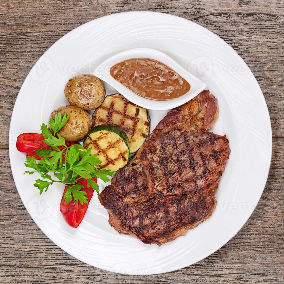 Grilled steaks, baked potatoes and vegetables on white plate 818846