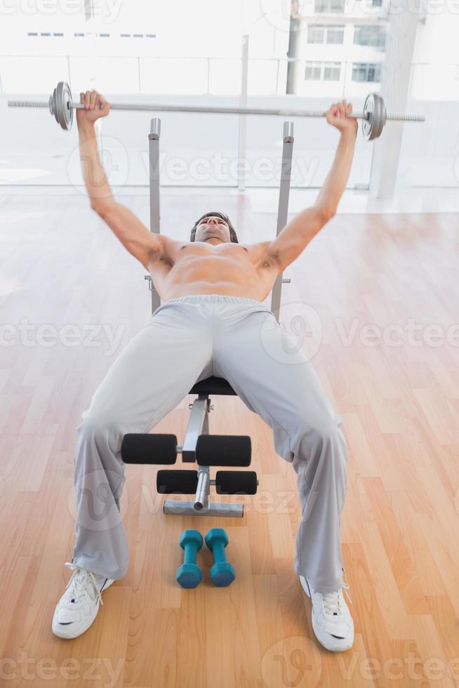 Fit man lifting barbell bench press in gym photo