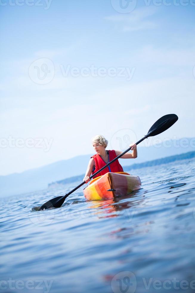 Woman With Safety Vest Kayaking Alone on a Calm Sea photo