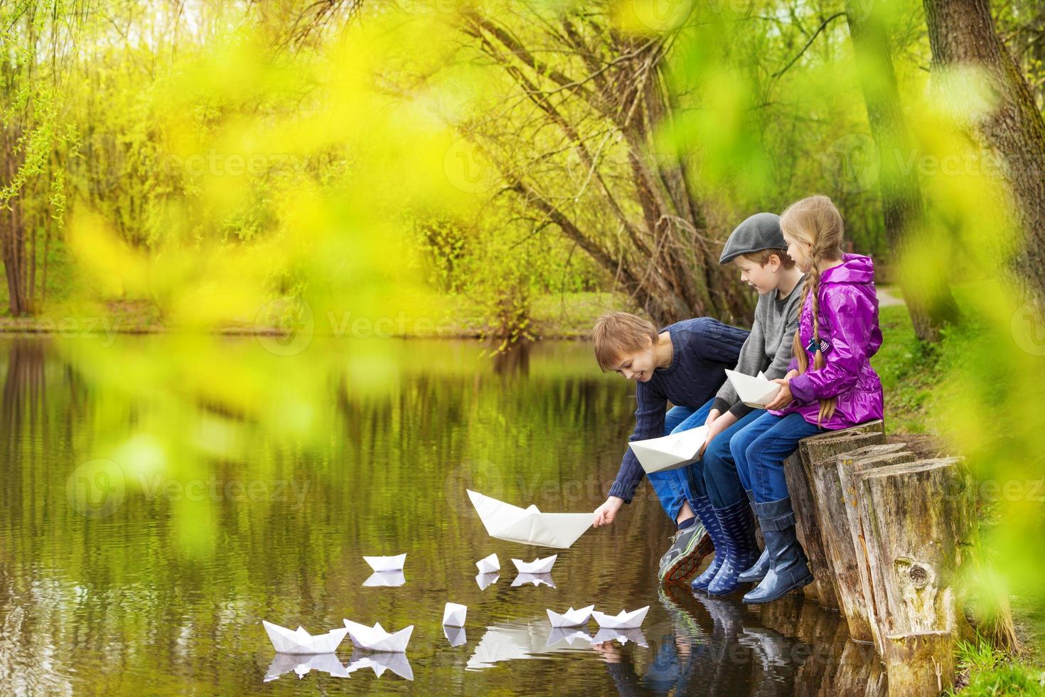 tres niños cerca del estanque poniendo barquitos de papel foto