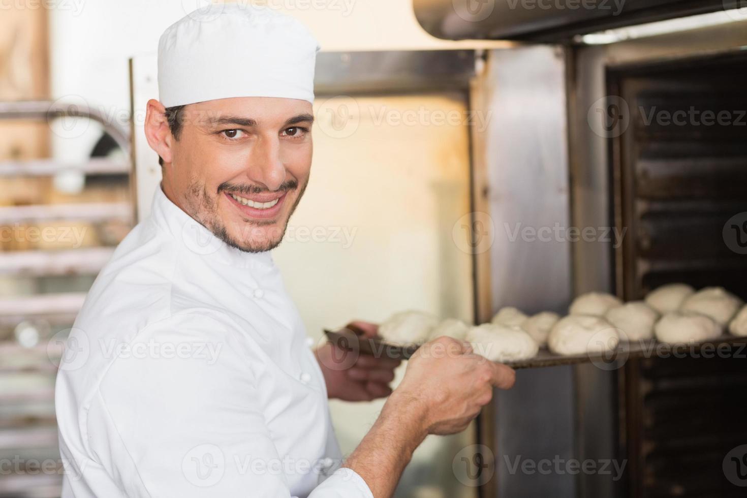 Smiling baker putting dough in oven photo