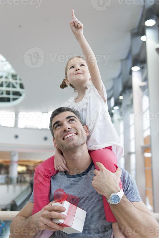 joven hija señala y se sienta sobre los hombros del padre foto
