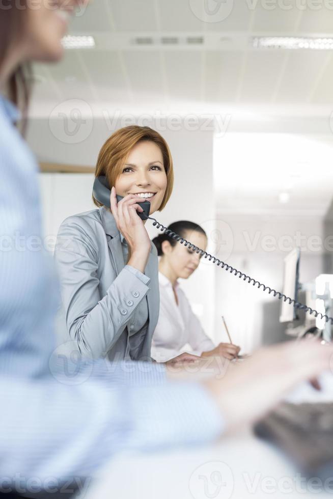 Smiling young businesswoman using landline phone in office photo