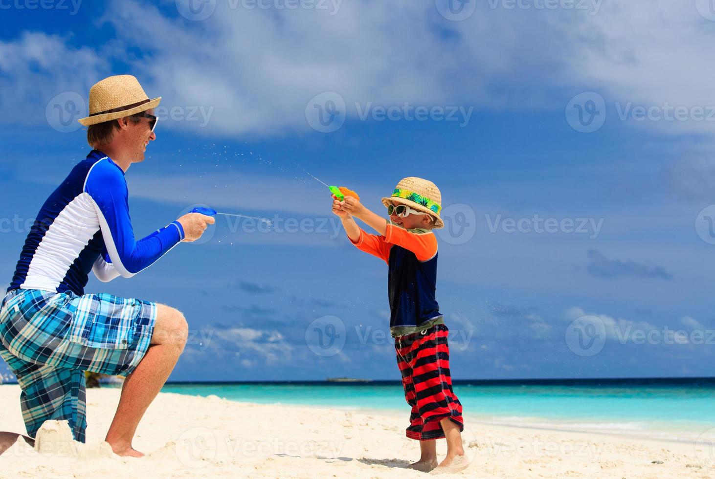 padre e hijo jugando con pistolas de agua en la playa foto