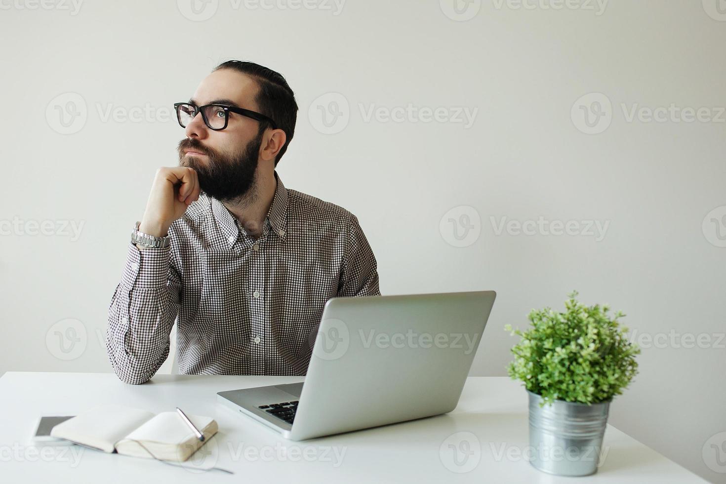 Hombre ocupado con barba en gafas pensando con laptop, smartphone foto