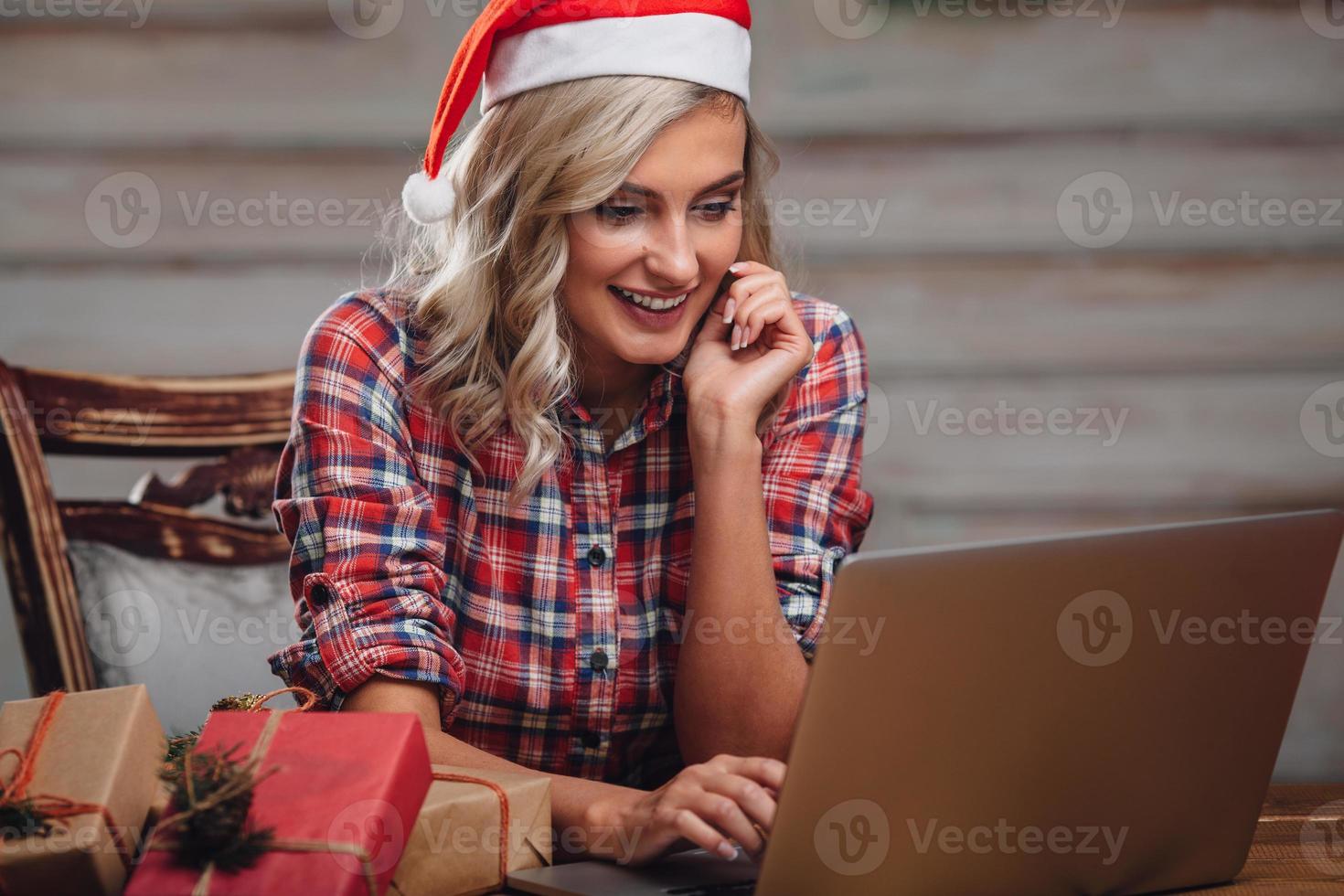 blonde woman wearing santa hat, working with laptop photo