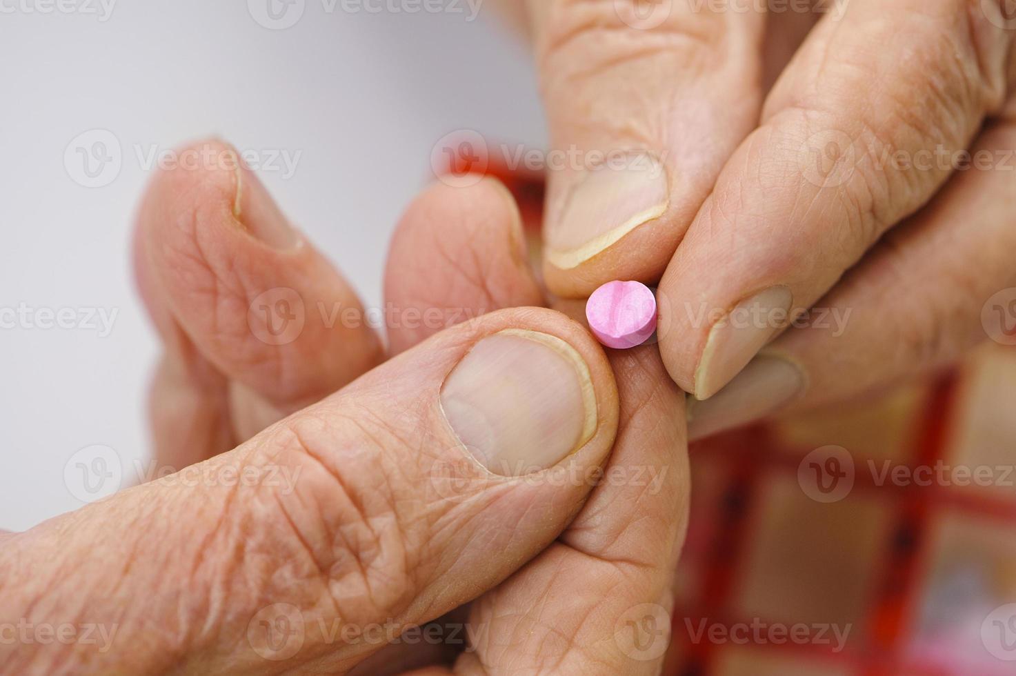 Elderly hands hold a pink tablet between the fingers photo