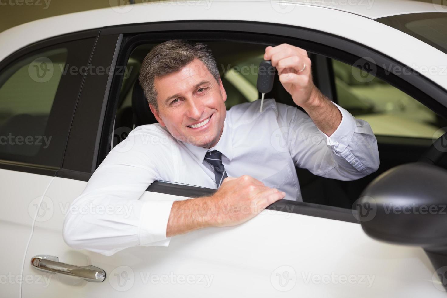 Hombre sonriente que sostiene la llave sentado en su coche foto