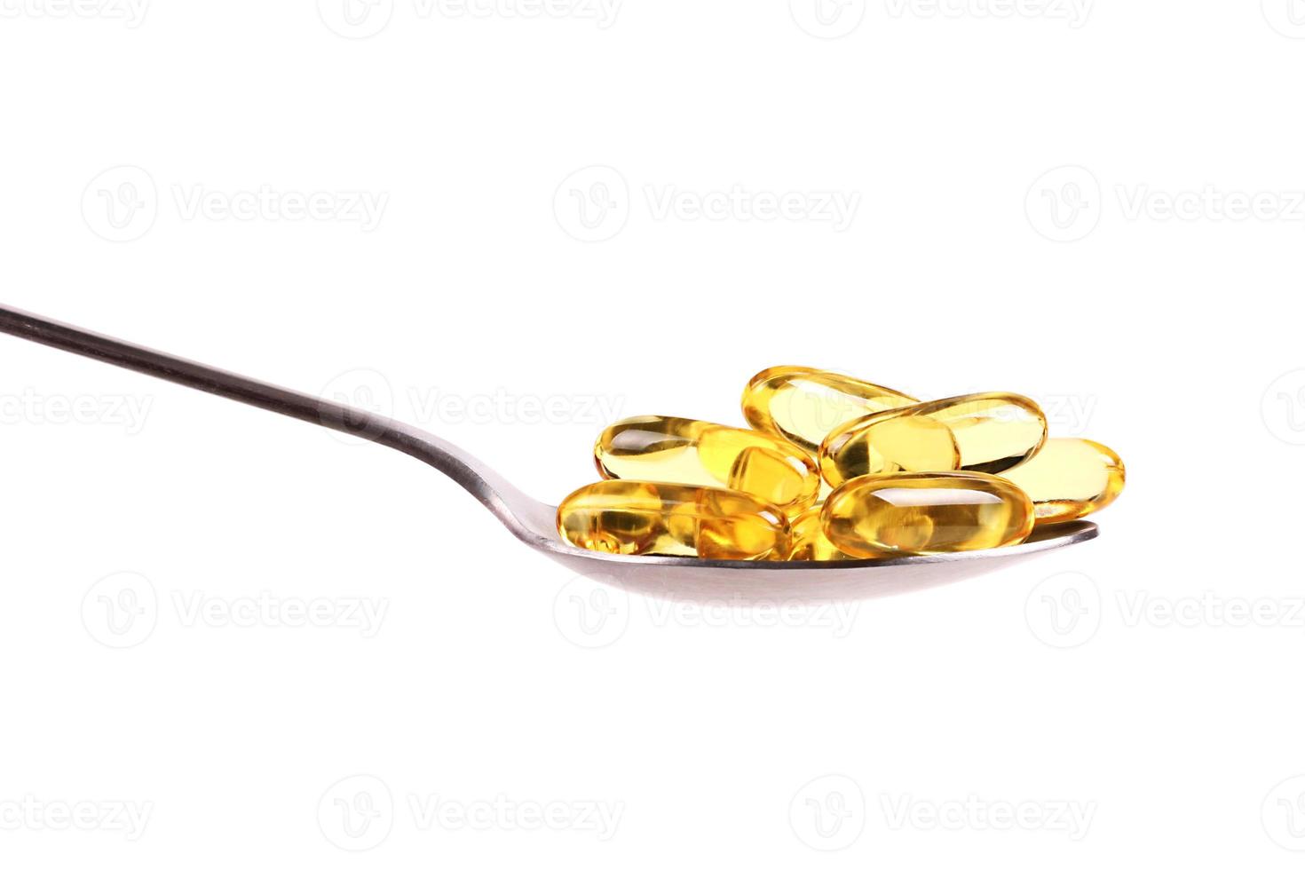 Spoon holding fish oil capsules isolated on white background photo