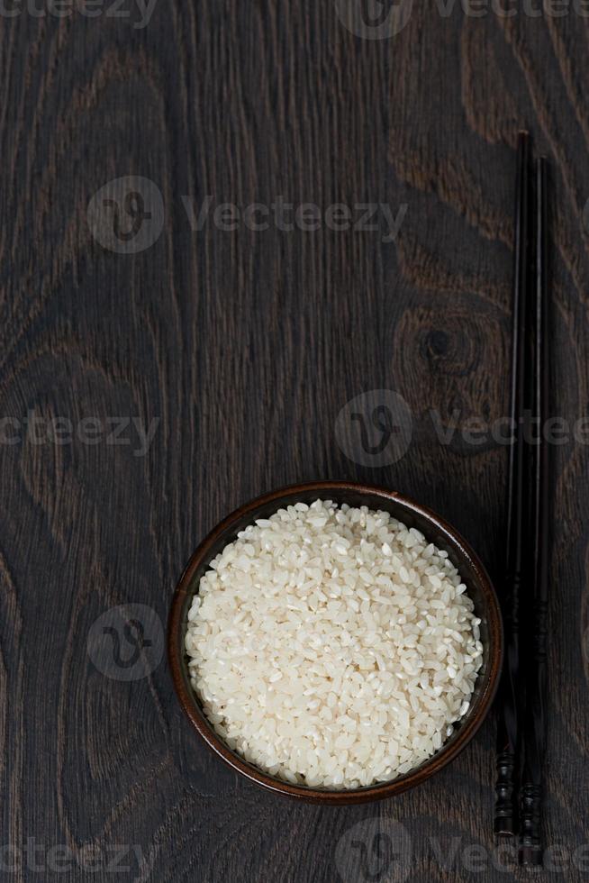 rice in bowl and chopsticks on dark background, top view photo