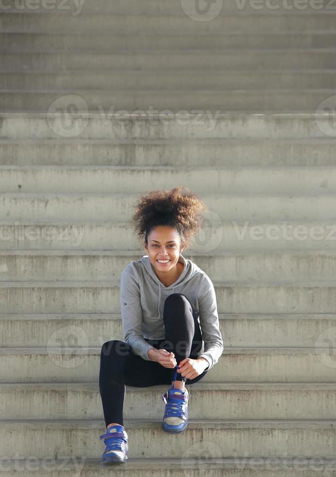 Sporty young woman sitting on steps tying shoe lace photo