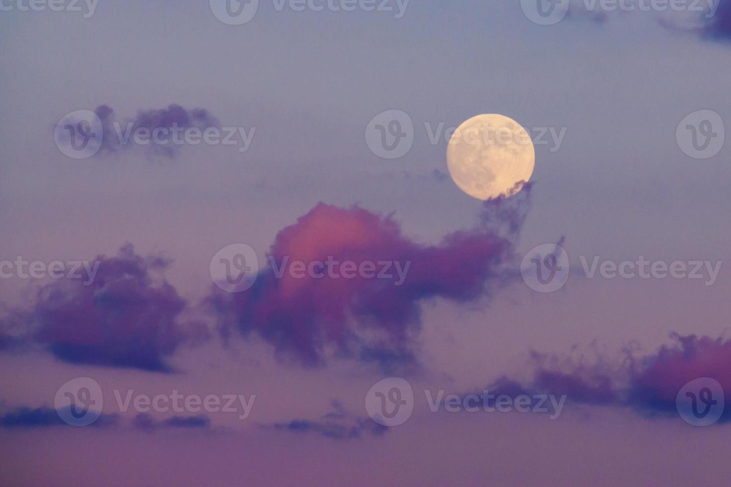 full moon rises through clouds in a purple night sky photo