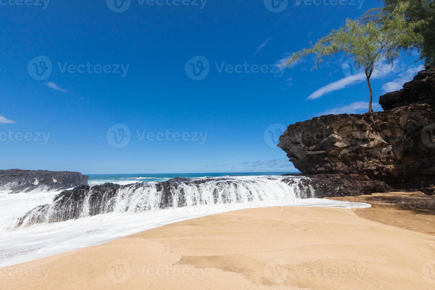 Waves splashing over lava rock on beautiful sandy tropical beach photo