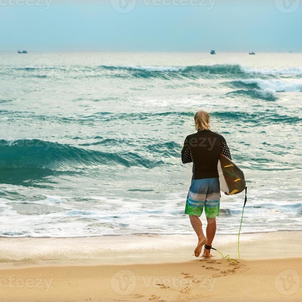 Surfer at the sea is standing with a surf board photo