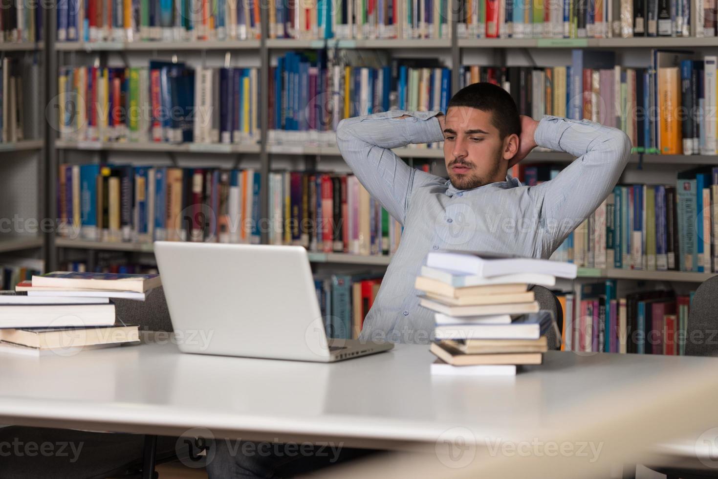 Un estudiante universitario masculino en una biblioteca mirando su computadora portátil foto