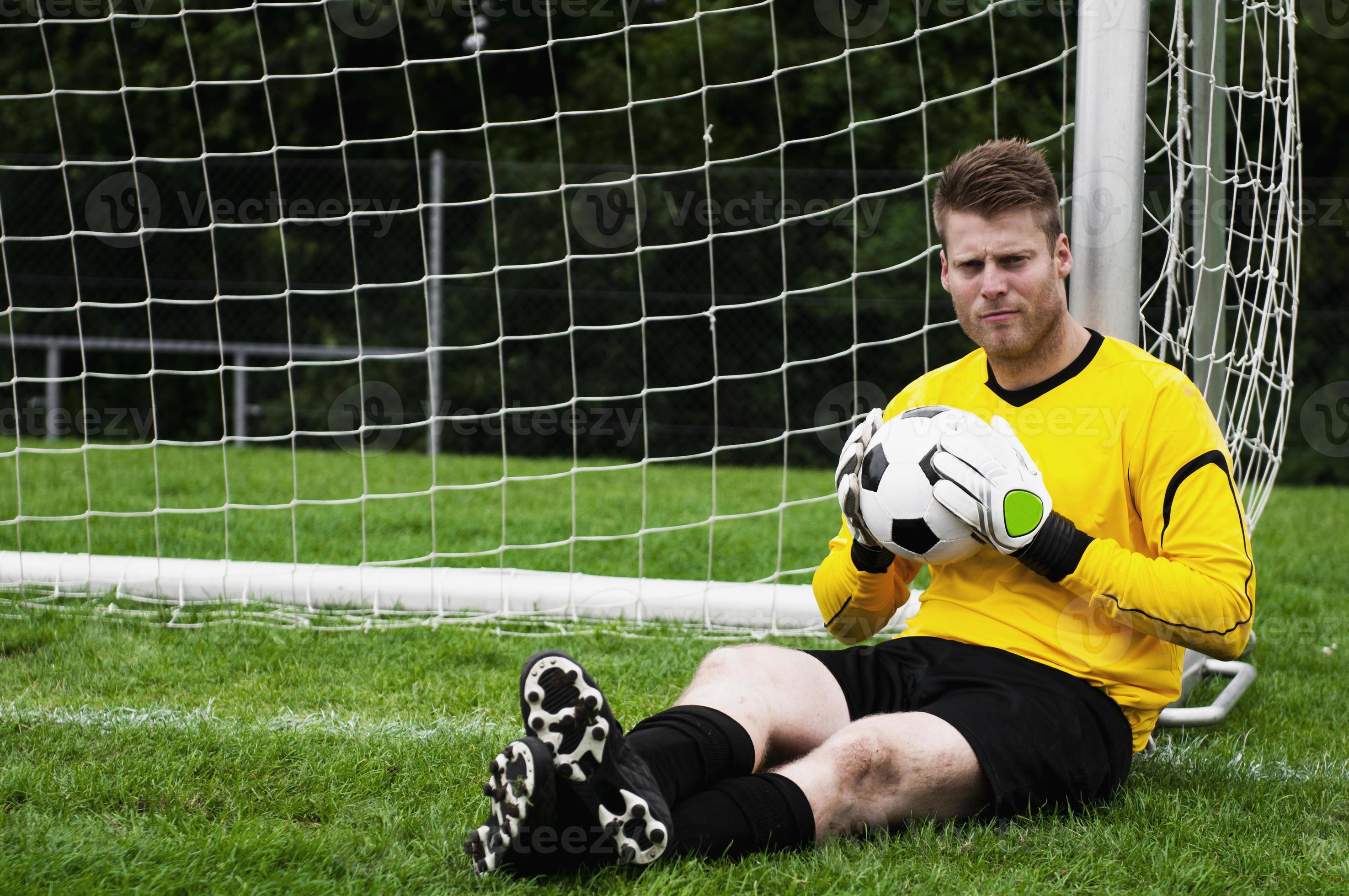 Portrait of relaxed goalkeeper sitting against goal post holding ball  897137 Stock Photo at Vecteezy